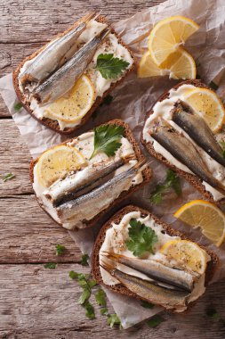Toasts with sprats, cream cheese and lemon close-up. Vertical to clipart
