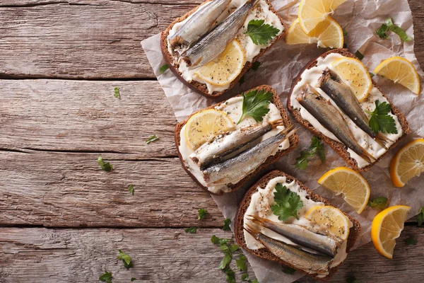 Toasts with sprats, cream cheese and lemon horizontal top view — Stock Image Toasts with sprats, cream cheese and lemon horizontal top view Stock Photo