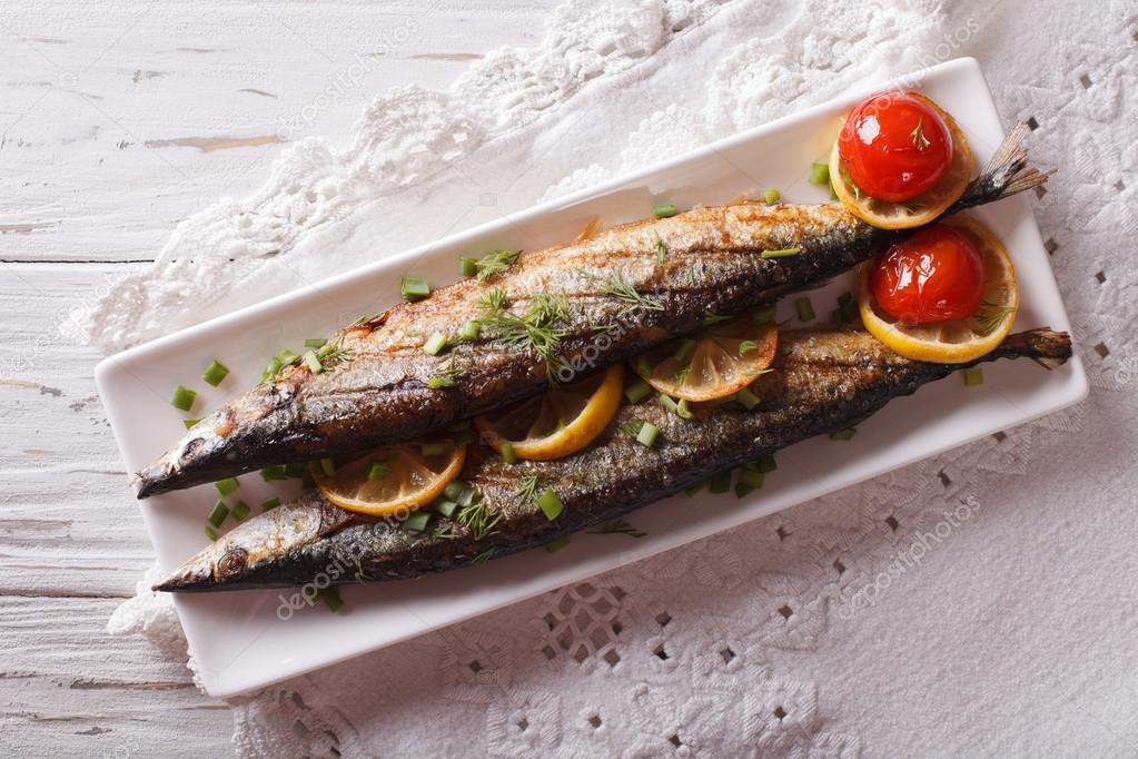 saury grilled with vegetables on a plate close-up. Horizontal to