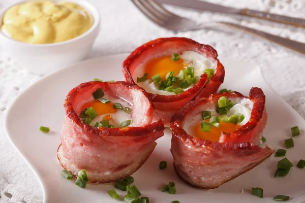 Fried eggs wrapped in bacon close-up on a plate and sauce. Horiz — Stock Photo, Image