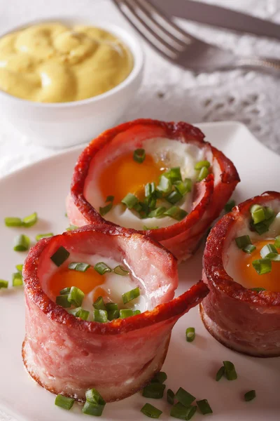 Fried eggs wrapped in bacon close-up on a plate and sauce. verti — Stock Photo, Image