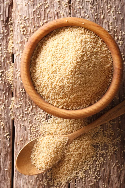 Raw Couscous in a wooden bowl and spoon close-up. vertical top v — Stock Photo, Image