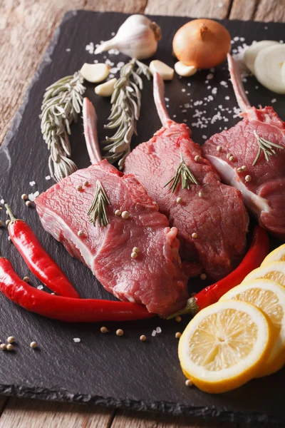 Biftecks de bœuf cru avec des ingrédients sur une planche d'ardoise en gros plan. Verti — Photo