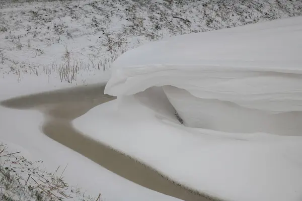 Ett tjockt lager snö som hänger över ett nästan fruset dike — Stockfoto