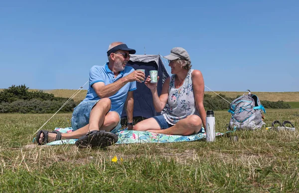 a mature elderly man and woman enjoying life having a picnic outside on a field with a cup of coffee
