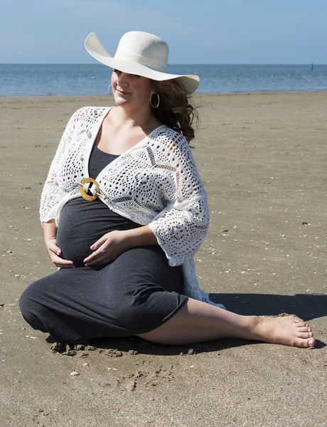Těhotná žena sedí na pláži — Stock fotografie