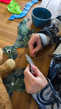 Genç zanaatkar, mavi pullar ve parlak yeşil kumaş kullanarak keçeli ejderha temalı bir parça dikiyor. Elle dikilen dikiş, yaratıcılık ve hayal gücünü rahat bir zanaat anında sergiliyor.