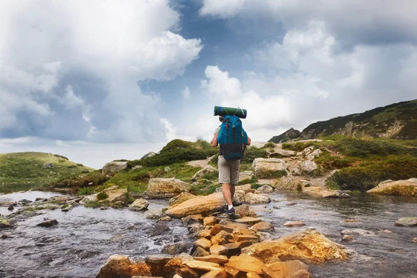 Hiker man with backpack crossing a river.