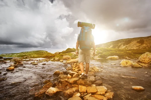 Wanderer überquert mit Rucksack einen Fluss. — Stockfoto