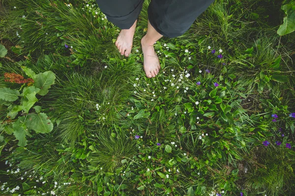 Γυναίκα στέκεται ξυπόλητος σε πράσινο γρασίδι και λουλούδια — Φωτογραφία Αρχείου