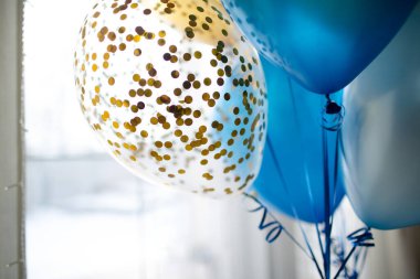 Parlak bir odanın şenlikli dekorasyonunda mavi ve şeffaf balonlar ve altın konfetiler. Tatilleri evde kutlarız. İç dekorasyon