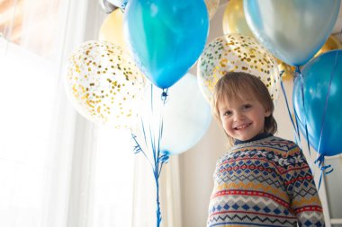 Bebeğin üçüncü doğum günü hediyesi. Şablonlu güzel kazaklı küçük bir çocuk balon tutuyor. İskandinav tarzında geniş pencereli parlak bir iç mekan