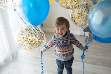 Bebeğin üçüncü doğum günü hediyesi. Şablonlu güzel kazaklı küçük bir çocuk balon tutuyor. İskandinav tarzında geniş pencereli parlak bir iç mekan
