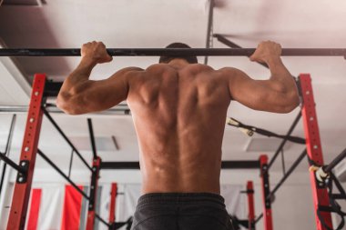 Çıplak gövdeli bir sporcunun fotoğrafı. Atletik bir adam kendini barın üzerine çekiyor..