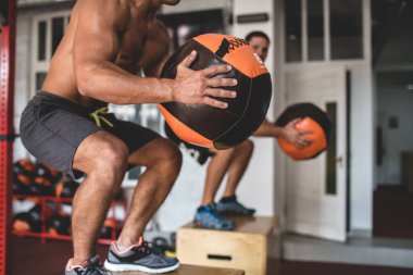 Çıplak gövdeli bir sporcunun fotoğrafı. Atletik yapılı bir adam bir medikal topla egzersiz yapıyor. Sporcu ve yoldaşı kaldırım taşına atlarlar.
