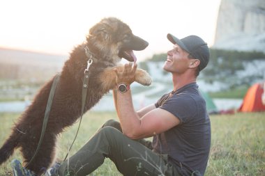 Sahibi ve evcil hayvanı çimlerin üzerinde oturuyorlar. Dağlarda kamp kurun. Köpek cinsi uzun saçlı çoban.