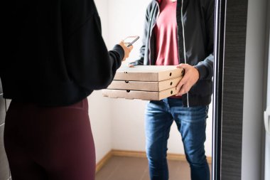 Pizza teslimatı telefon uygulaması konsepti. Ev kapısındaki yemek dağıtıcısı ve müşterisi cep telefonuyla internet üzerinden ödeme, bahşiş ya da değerlendirme yapıyor. İtalyan restoranının fast food kutuları..