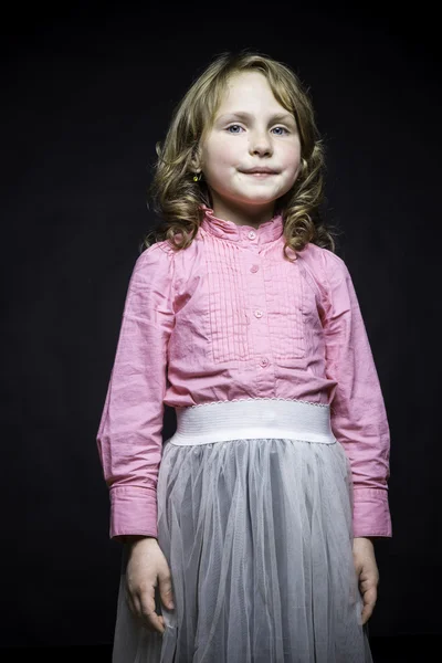 Bella bambina in una camicetta rosa e gonna bianca su uno sfondo nero strutturato — Foto Stock