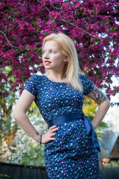 Chica rubia joven en el estilo Pin-up chica en un vestido azul en el jardín florecido — Foto de Stock