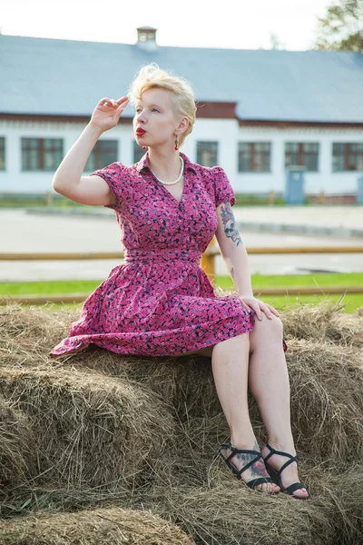 Belle fille blonde dans le style pin-up dans une robe lumineuse sur le foin — Photo