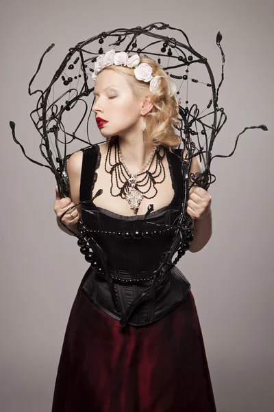 Beautiful young blonde girl with black tears in Gothic black corset and red skirt with artificial white roses in her hair — Stock Photo, Image