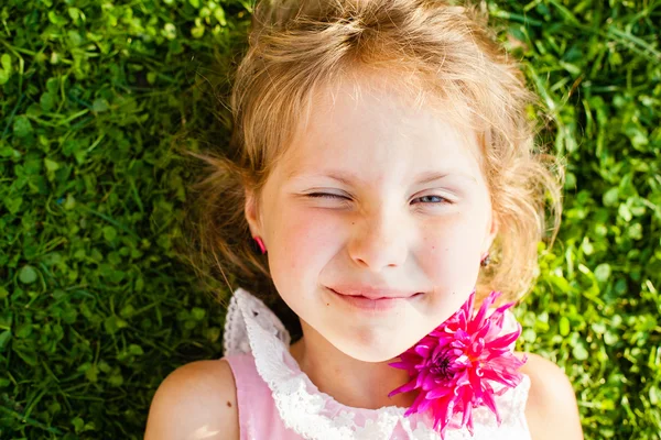 Linda menina loira de olhos azuis deitada na grama com uma flor nas mãos — Fotografia de Stock