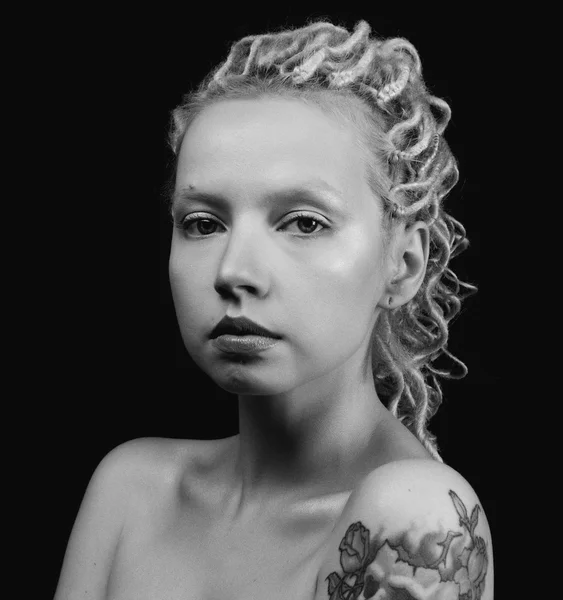 Belle jeune femme blonde avec de minces dreadlocks bouclés et un tatouage sur son avant-bras — Photo