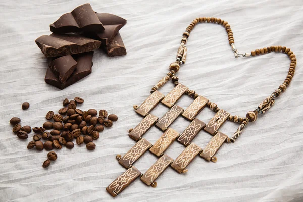 Ethnic beads, coffee beans and pieces of chocolate on a white tablecloth — Stock Photo, Image