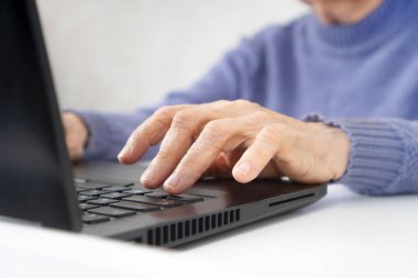 Dizüstü bilgisayarda yazan buruşuk elleri olan yaşlı bir kadın.