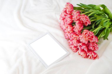 Yumuşak battaniyenin üzerinde pembe şakayık laleleri buketinin yanında boş bir maket var.. 