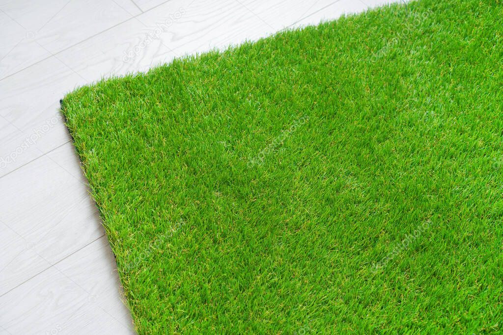 Soft artificial grass carpet lying on the white wooden floor