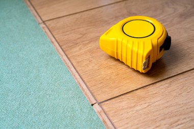 Yüksek kaliteli lamine zemin kurulumu. Kaplama için doğal süsleme. Sarı mezura üstte duruyor..