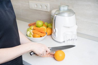 Mutfak bıçaklı kadın, elmadan, portakaldan ve havuçtan yapılmış taze bir meyve suyu hazırlamak için portakalı kesiyor..