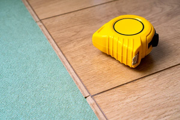 Yüksek kaliteli lamine zemin kurulumu. Kaplama için doğal süsleme. Sarı mezura üstte duruyor..