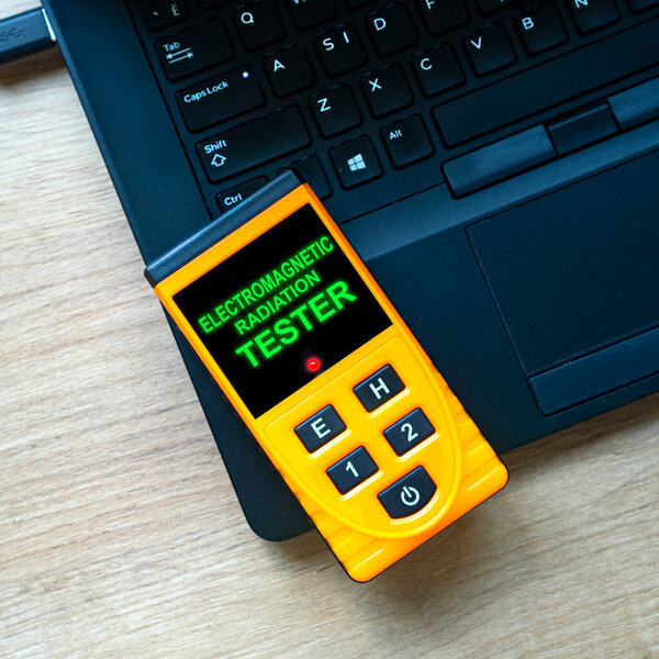 Измерение электромагнитного излучения на рабочем месте дома или в офисе. Ваше рабочее место в безопасности? Тестер электромагнитного излучения лежит на ноутбуке. Площадь композиции.