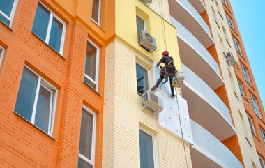 Yüksek binalı inşaatçı çok katlı bir binanın dış cephesini yalıtıyor..
