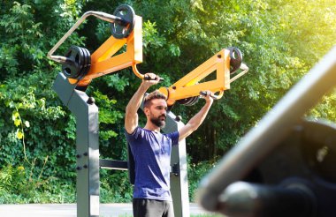 Genç sakallı atletik adam sokak eğitim aletleri üzerinde egzersiz yapıyor.. 