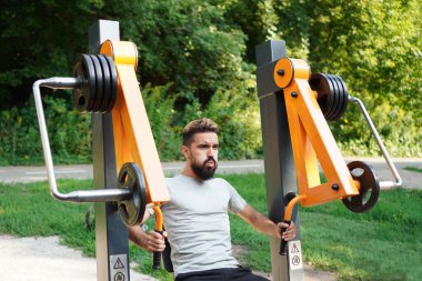 Spor salonu aç. Belediye spor ekipmanları üzerine sokak eğitimi. Karizmatik adam açık hava eğitim makinesini itiyor.. 