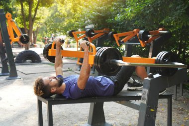 Atletik adam açık hava antrenman makinesini kullanarak göğüs presi yapıyor. Spor salonu aç. Belediye spor simülatörleri üzerine sokak eğitimi.