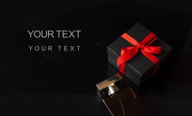 Siyah hediye kutusunun yanındaki parfüm şişesinde kırmızı kurdele var. Kara Cuma indirimi, Noel hediyesi ya da Sevgililer Günü hediyesi konsepti. Kopyalama alanı olan pankart.