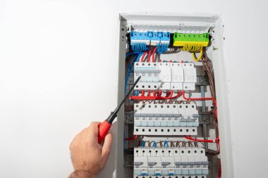 Elektrikçi, elektrik paneli üzerinde çalışırken tornavida kullanıyor. Modern binada profesyonel bakım ve güç dağıtım sistemi onarımı.