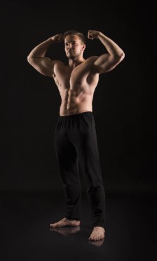 Güçlü atletik adam çıplak kaslı vücudunu gösteriyor. Karanlık bir arkaplanda stüdyo çekimi.