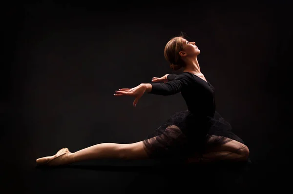 Charming girl ballerina in a black suit, is dancing a ballet in the light of the contour . Shooting a performance on a dark background.