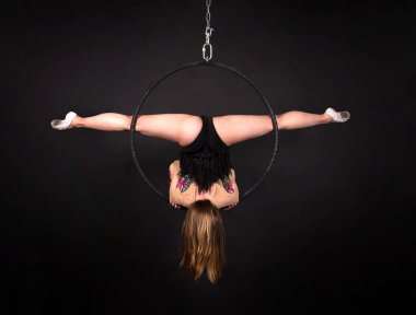 Koyu renk bir takım elbiseyle hava akrobasisi yapan genç bir kadın karanlık bir arkaplanda hava halkasıyla egzersiz yapıyor. Stüdyo çekimi.