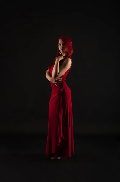 一个红头发的女孩 穿着红色的衣服 在深色的背景上摆姿势 工作室拍摄 — 图库照片