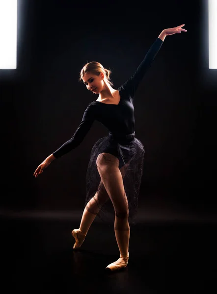 Charming girl ballerina in a black suit, is dancing a ballet in the light of the contour . Shooting a performance on a dark background.