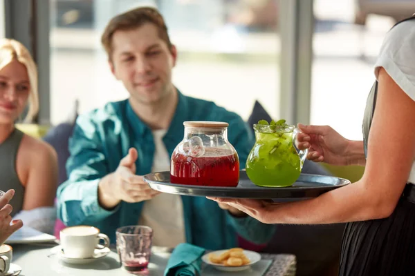 Приємний офіціант дає напої на лотку клієнтам — стокове фото