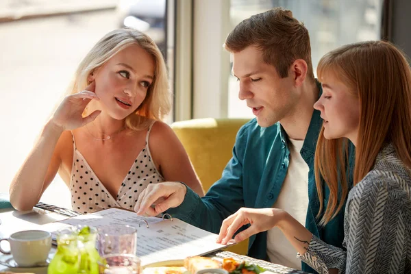 Три колеги в кафе обговорюють їжу в меню — стокове фото