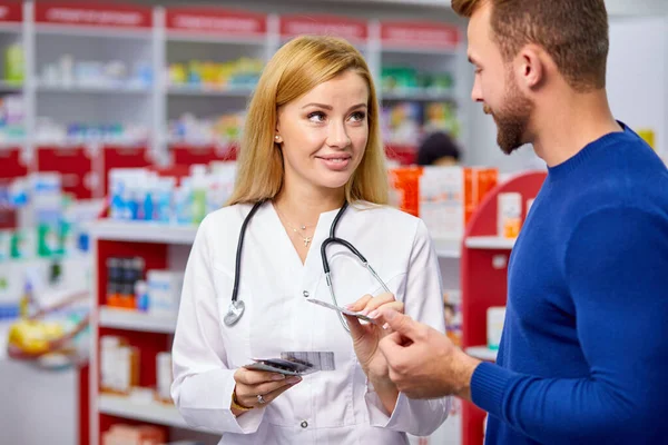 Professional female pharmacist helping male customer choosing prescription drugs — Stock Photo, Image