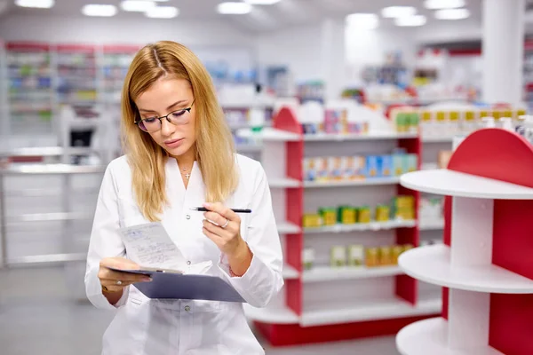 Młoda, ładna kobieta farmaceuta poszukuje lekarstw na półkach aptecznych — Zdjęcie stockowe
